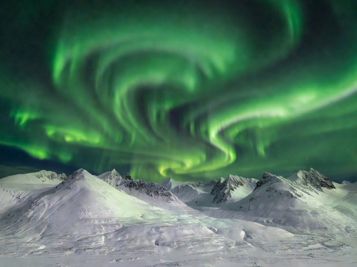 Spectacular green Aurora Borealis swirling over snow clad peaks in Tromso Norway